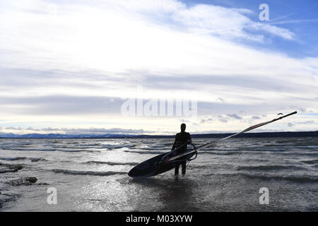 Herrsching, Germania. 18 gennaio, 2018. Il surfer Dominik wades nell'tumultous acqua con la sua tavola da surf come la tempesta 'Friederike' infuria in tutta la Germania, in Herrsching, Germania, 18 gennaio 2018. Credito: Felix Hörhager/dpa/Alamy Live News Foto Stock