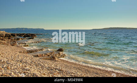 Spiaggia con le rocce vulcaniche e ciottoli lungo il mare Adriatico con le isole in background su Mali Losinj Island, Croazia Foto Stock