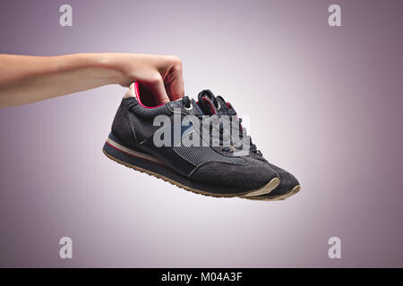 Mano che tiene un vecchio Dirty Sneaker Scarpa Foto Stock