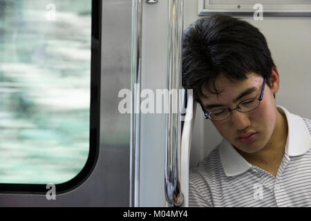 Un giovane giapponese studente maschio dormire all'interno di un treno in Tokyo, Giappone, vicino a una finestra Foto Stock