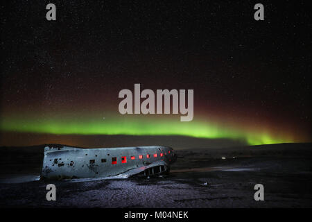 Aurora boreale, o luci del nord, brillano sopra il piano relitto di un US Navy aereo - un Super Douglas DC-3 - sulla spiaggia nera di Solheimasandur, sud dell'Islanda. Foto Stock