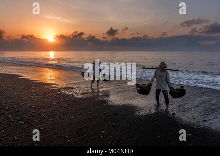 Sale indonesiano agricoltore di Kusamba sale villaggio minerario di Bali la raccolta di acqua di mare al mattino per la produzione di sale utilizzando il metodo tradizionale Foto Stock