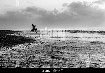 Sale indonesiano agricoltore di Kusamba sale villaggio minerario di Bali la raccolta di acqua di mare al mattino per la produzione di sale utilizzando il metodo tradizionale Foto Stock