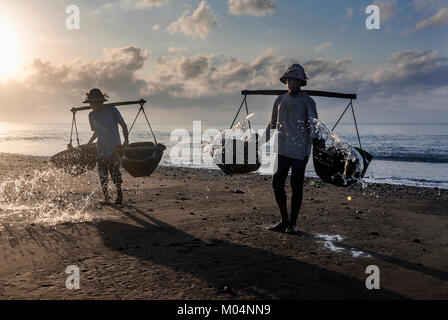 Sale indonesiano agricoltore di Kusamba sale villaggio minerario di Bali la raccolta di acqua di mare al mattino per la produzione di sale utilizzando il metodo tradizionale Foto Stock