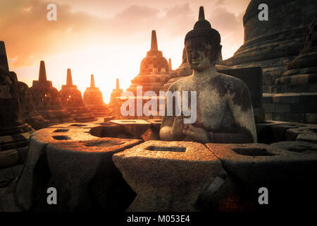 Incredibile vista sunrise di meditare la statua di Buddha e stupa di pietra contro il sole splendente su sfondo. Il Borobudur antico tempio buddista. Grande religiou Foto Stock