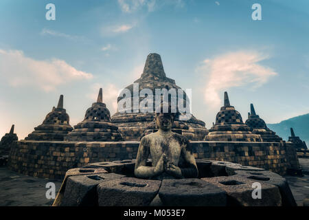 Incredibile statua del Buddha meditando e stupa di pietra contro il cielo blu su sfondo. Il Borobudur antico tempio buddista. Grande architettura religiosa. Foto Stock