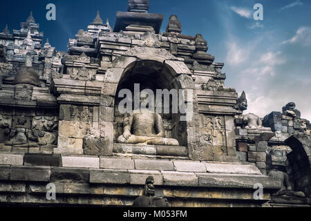 Incredibile scolpita la statua di Buddha seduto in posizione di meditazione contro il cielo blu su sfondo. Il Borobudur antico tempio buddista. Grande religioso arch Foto Stock