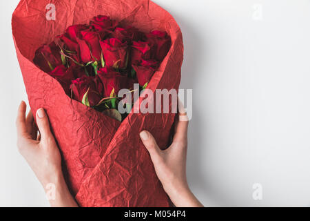 Vista parziale di donna holding bouquet di rose rosse in carta di avvolgimento per san valentino isolato su bianco Foto Stock