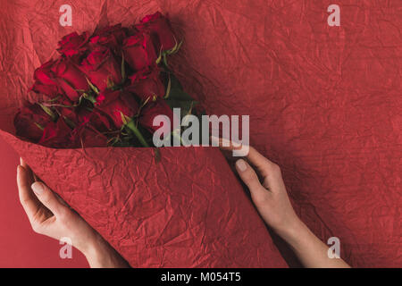 Vista parziale di donna holding bouquet di rose rosse in carta di avvolgimento per San Valentino Foto Stock