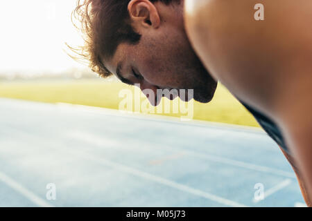 Primo piano di un velocista in piedi su una via di corsa. Stanco atleta rilassante dopo una corsa in piedi sulla pista con gli occhi chiusi. Foto Stock