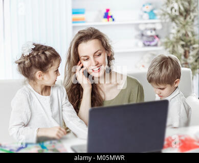 Giovane madre - business donna che lavorano su laptop e parlare sullo smartphone al fianco dei loro figli Foto Stock