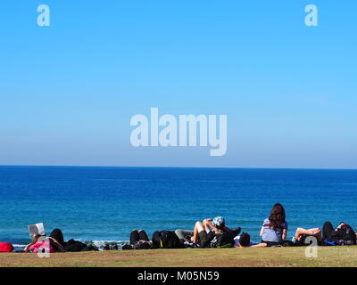 Gruppo di amici sdraiati al sole e relax divertimento presso il lungomare vicino alla spiaggia di fronte al mare su una giornata perfetta con cielo blu chiaro Foto Stock