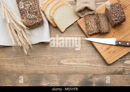 Tagliare a fette e grano intero pane su una tavola di legno. Un filone di rustico fresco intero pasto pane di segale, tagliati su una tavola di legno, alimentari rurale dello sfondo. Foto Stock