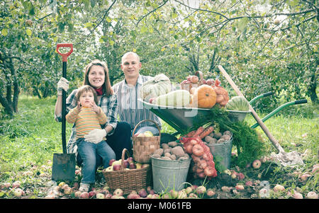 Felici i genitori e il bambino con ortaggi raccolti in giardino Foto Stock