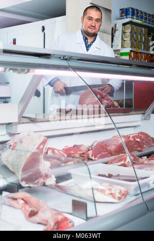 Maschio il personale del negozio in tunica bianca la vendita di carne halal al bancone Foto Stock