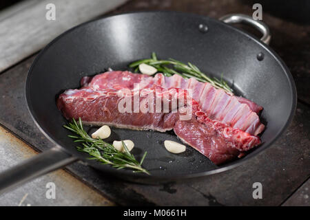 Fried costolette di agnello. aggiungere un rametto di rosmarino e aglio. La cottura con il fuoco in padella. Professionale chef nella cucina del ristorante la cucina. L uomo per frittura in Padella fiammante sul piano di cottura. Foto Stock