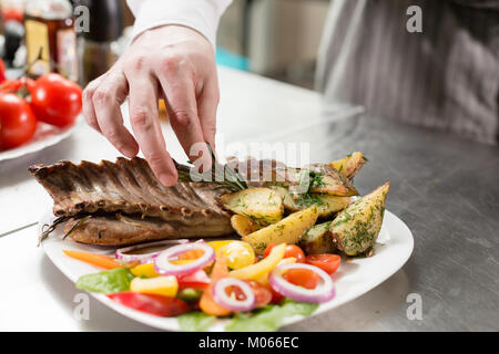 Lo chef prepara nel ristorante. Grigliata di carré di agnello con patate fritte e verdure fresche closeup Foto Stock