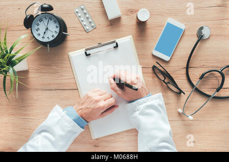 Vista aerea del medico maschio scrivere le note mediche del paziente o di storia della medicina prescrizione sulla carta per appunti durante esame medico in ospedale offi Foto Stock