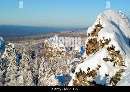 Vista dalla parte superiore della cresta degli Urali in una limpida giornata invernale sulle colline boscose e rocce in primo piano Foto Stock