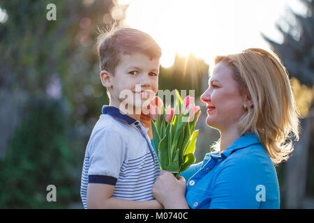 Piccolo figlio dà bouquet di tulipani di mamma a giornata della madre in sunset Foto Stock