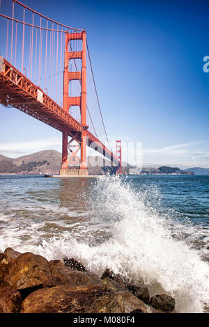 Golden Gate Bridge di San Francisco. Vista da massi di seguito con gli spruzzi di onde in primo piano. In verticale Foto Stock