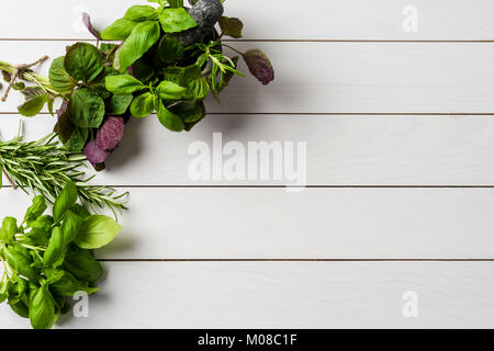 Mazzetti di erbe aromatiche fresche con mortaio e pestello su bianco tavolo in legno Foto Stock