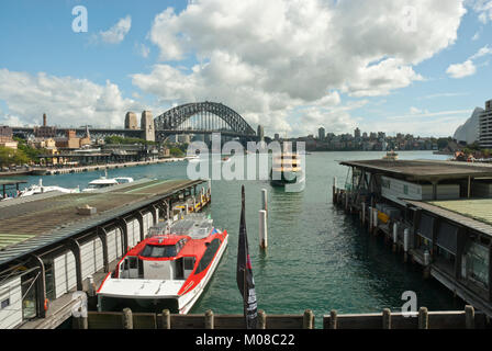 Il Circular Quay con traghetti di Sydney e il Sydney Harbour con Sydnay Harbour Bridge in background. La molla/giorno di estate, sole, cielo blu, soffici nuvole. Foto Stock