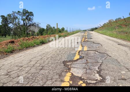 Strada danneggiata di Yokohl Drive in California, Stati Uniti d'America - Asfalto Screpolato asfalto con buche e le patch Foto Stock