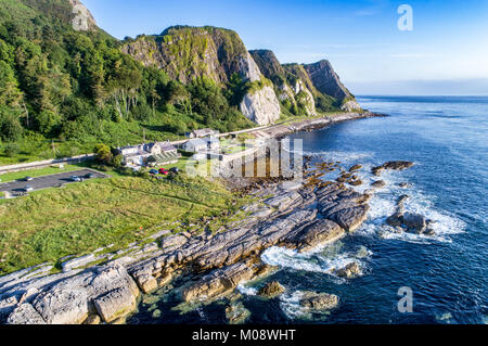 La costa orientale dell'Irlanda del Nord con scogliere, rocce e costiera di Antrim Road, a.k.a. Causeway percorso costiero, case e parcheggio. Vista aerea Foto Stock