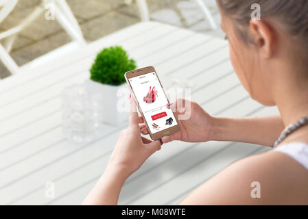 Donna shopping online con smart phone. Ricerca per scarpe da donna. Coffee shop tabella in background. Foto Stock