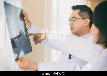 Due medico parlando e sta esaminando la pellicola a raggi x circa il risultato e la sfocatura dello sfondo in sala operatoria con raggi X di scansione medico in ospedale. Foto Stock