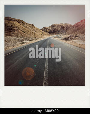 Un vuoto che la strada asfaltata che attraversa zone aride montagne nel Sultanato di Oman in Al Wusta Governate (vintage Polaroid con telaio effetto) Foto Stock