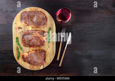 Una foto aerea di tre fette di carne cotta, filetti di manzo, ripresa dall'alto sul buio rustica con rametti di rosmarino, sale, pepe, vino, Foto Stock