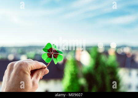 Primo piano di una foglia di quattro Lucky Clover detenute da un lato contro la skyline come modello Foto Stock