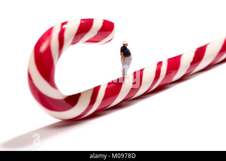 Conceptual close-up di una miniatura uomo grasso con disturbi alimentari in piedi su un rosso di canna da zucchero contro uno sfondo bianco per lo spazio di copia Foto Stock