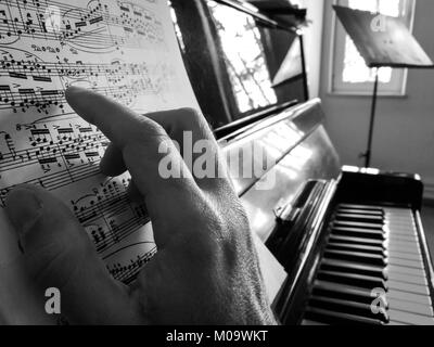 Un maschio di mano è su un pianoforte spartiti di toccare la carta come egli è in riproduzione. Un piano acustico e un music stand in background. Foto Stock