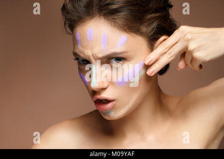 La risoluta donna fare il trucco con correttore. Foto di bella bruna donna su sfondo marrone. Cura della Pelle concept Foto Stock