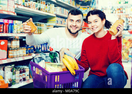 Piacevole giovane in piedi vicino a ripiani con conserve di merci in negozio Foto Stock
