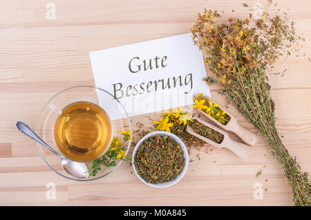 Biglietto di auguri con una tazza di tè con secca e fresca erba di San Giovanni e la carta bianca con testo tedesco: ottenere ben Foto Stock