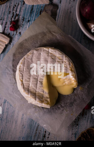 Foto verticale con vista dall'alto sulla singola camembert arrosto con la pelle bianca. Piccolo pezzo è tagliato e il formaggio viene parzialmente fuso. Il formaggio è su pape Foto Stock