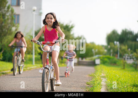 Tre bambini felici equitazione sulla bicicletta e acooter Foto Stock