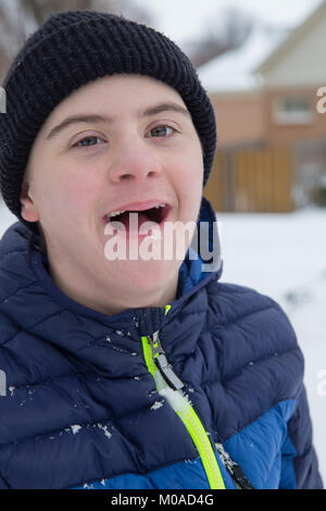 Felice ragazzo adolescente con autismo e sindrome di Down giocare al di fuori nella neve Foto Stock