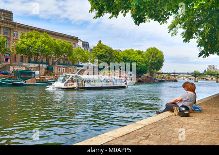 Parigi, Francia - 15 Maggio 2017: giovani seduta dal fiume Senna in corrispondenza della punta della Ile de la Cite isola come le navi da passeggeri di passare loro. Parigi è th Foto Stock