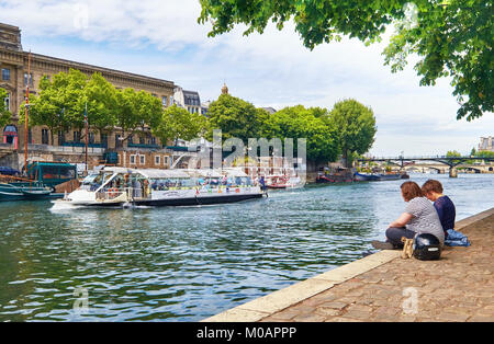 Parigi, Francia - 15 Maggio 2017: giovani seduta dal fiume Senna in corrispondenza della punta della Ile de la Cite isola come le navi da passeggeri di passare loro. Parigi è th Foto Stock