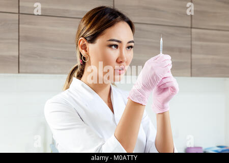 Close-up giovane donna azite medico estetista in bianco camice e guanti sterili prepara la siringa per iniezione di Botox Foto Stock