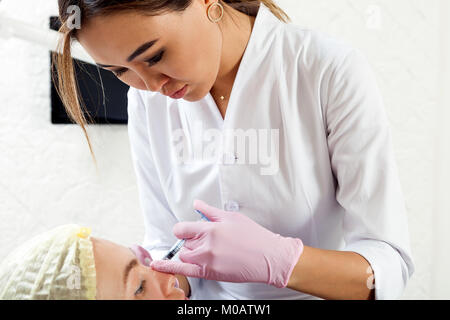 Close-up di una donna azian estetista in un medico vestaglia e guanti sterili rende una donna iniettare Botox Foto Stock