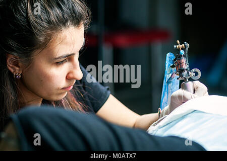 Close-up di una bella tatuaggio donna facendo un tatuaggio con un tatuaggio macchina da una giovane donna sulla sua coscia in un salotto tattoo Foto Stock