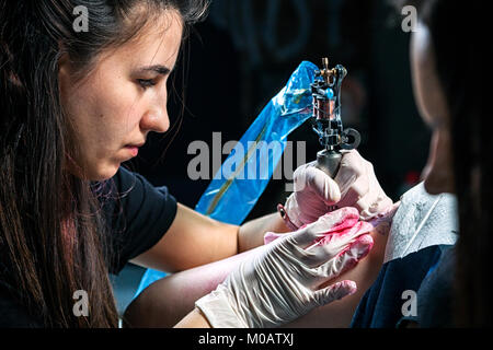 Una bella tatuaggio donna fa un tatuaggio di un piccolo uccello con vernice rossa con un tatuaggio macchina da una giovane donna sul suo hip Foto Stock
