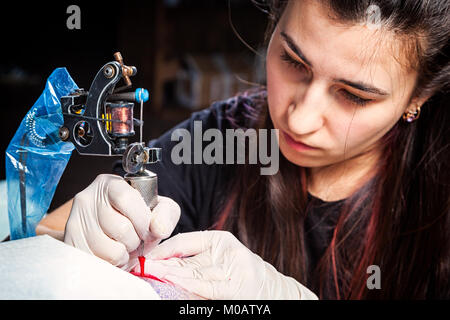 Close up tattoo artist dimostra il processo di getting tattoo rosso. Foto Stock