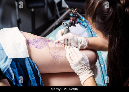 Tattooer donna che mostra il procedimento di preparazione di un tatuaggio uccello sulla donna. Tattoo design pattern in Foto Stock